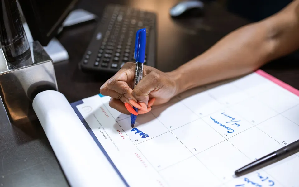 Una persona anota fechas en un calendario de escritorio con un rotulador azul